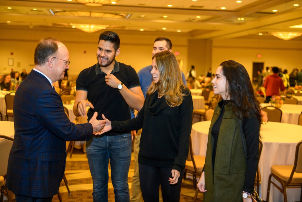 President DeGioia speaks with a group of 4 students in the Thanksgiving Dinner dining hall.