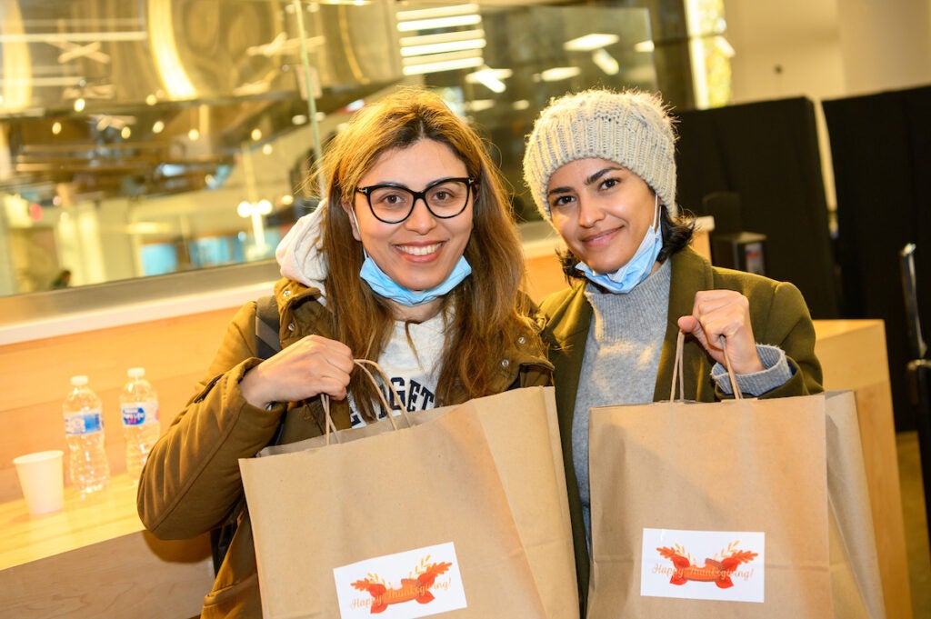 Two students pose with bags filled with their Thanksgiving Day to-go meals. This photo is from 2021, during the height of the Covid-19 pandemic.