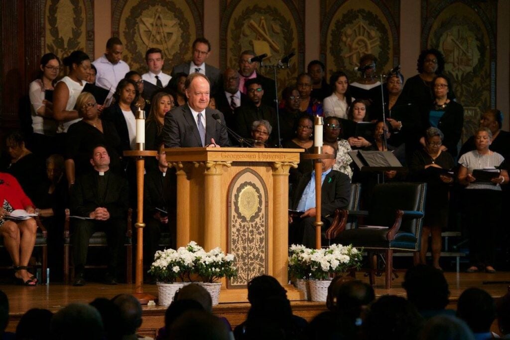 President DeGioia speaks to a large audience from an ornate wooden podium in Gaston Hall.