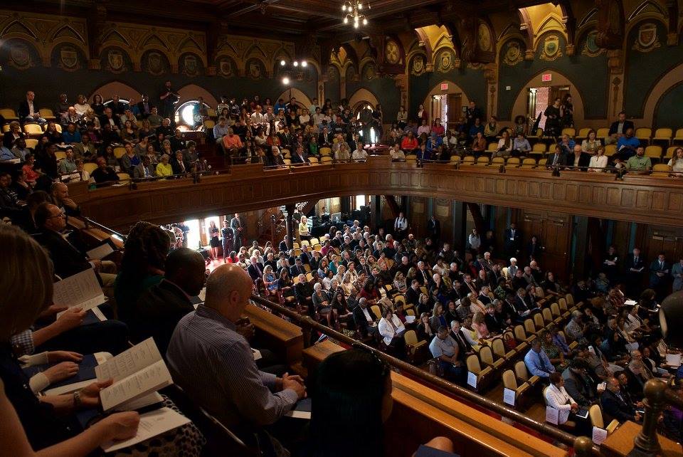 Wide shot of a large seated crowd in Gaston Hall, which features a full bottom level with an upper balcony.