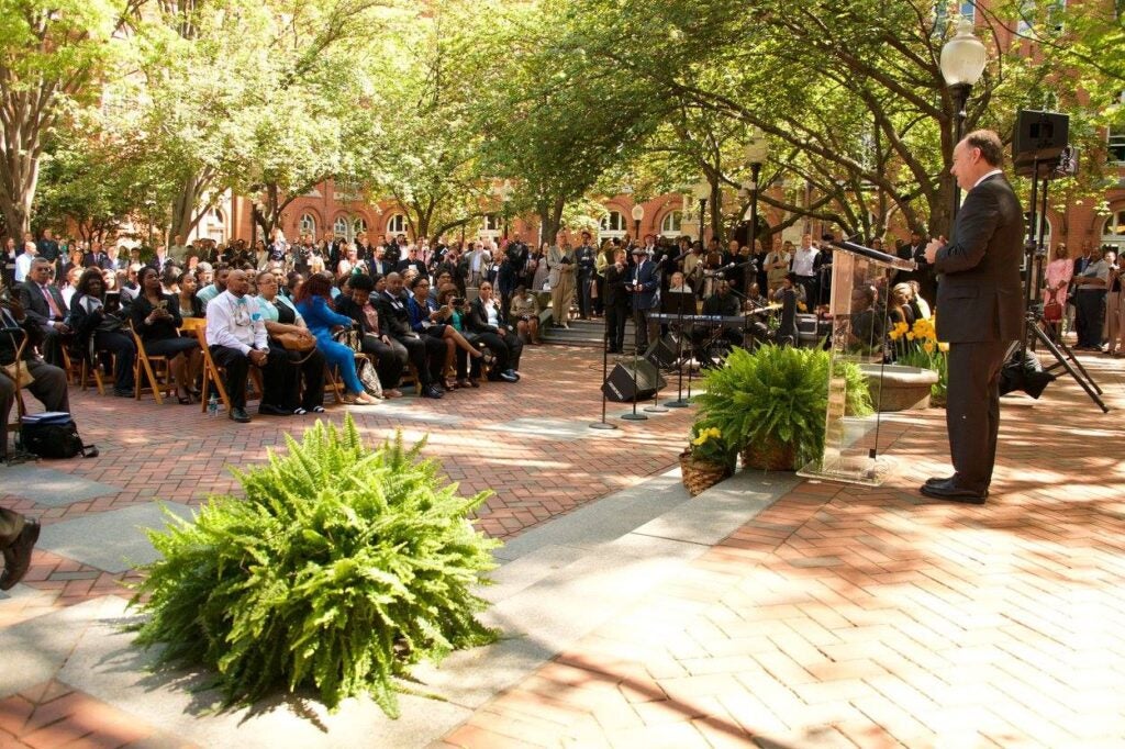 President DeGioia stands outside the newly renamed Hawkins Hall, addressing a seated audience.