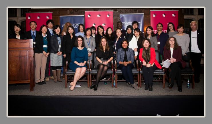 A large group of men and women pose for the camera on a stage with a backdrop of Georgetown University and HeForShe banners.