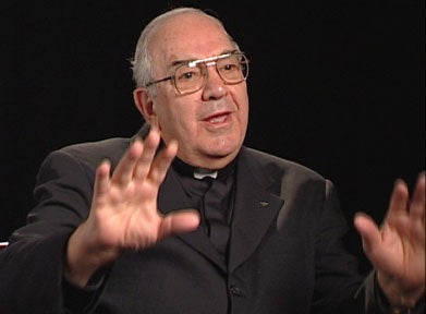 Dominic Maruca, S.J., a white man with greying hair and glasses, wearing a clergy collar and dark suit jacket.