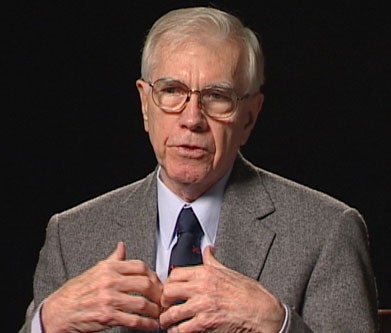 Joseph Tetlow, S.J., a white man with greying hair and glasses, wearing a light blue collared shirt and dark tie with a medium grey suit jacket.