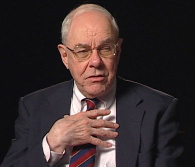 John Padberg, S.J., a white man with grey hair and glasses, wearing a white collared shirt and red tie with a dark suit jacket.