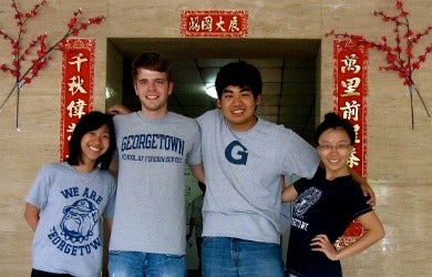 Four students wearing Georgetown University t-shirts stand outside an entrance with Chinese writing.