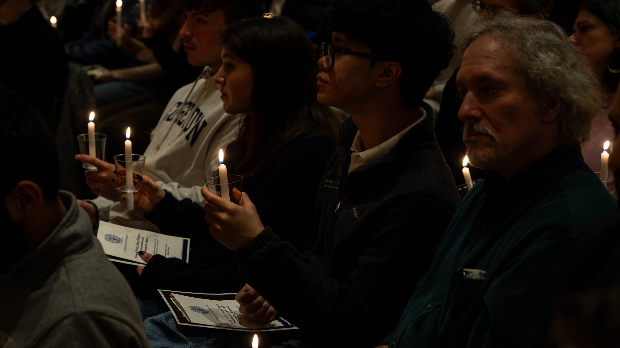 A group of people sitting in a dark chapel, holding vigil candles.