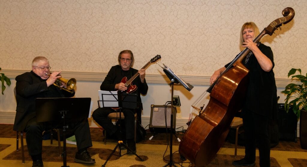 A three-piece band, consisting of a trumpet player, guitarist, and upright cellist, perform at the Thanksgiving Dinner.