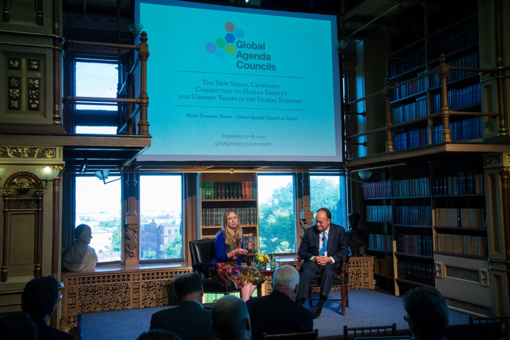 John J. DeGioia and Chelsea Clinton are seated in Riggs Library, speaking in front of an audience.