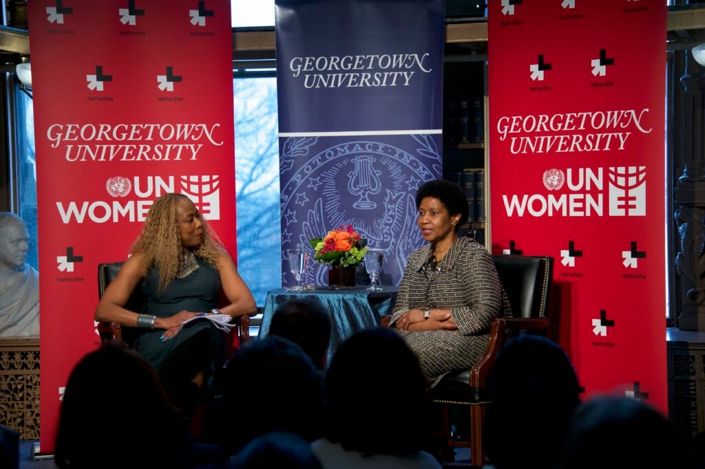 Two black women sit in front of an audience in a panel discussion. Behind them are Georgetown University UN Women banners, marking the HeForShe campaign launch.