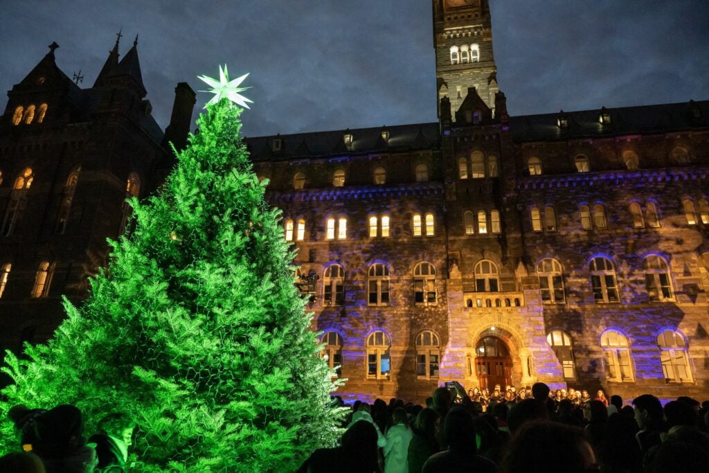 A lit up Christmas tree, topped with a brightly lit white star, stands in front of Healy Hall.