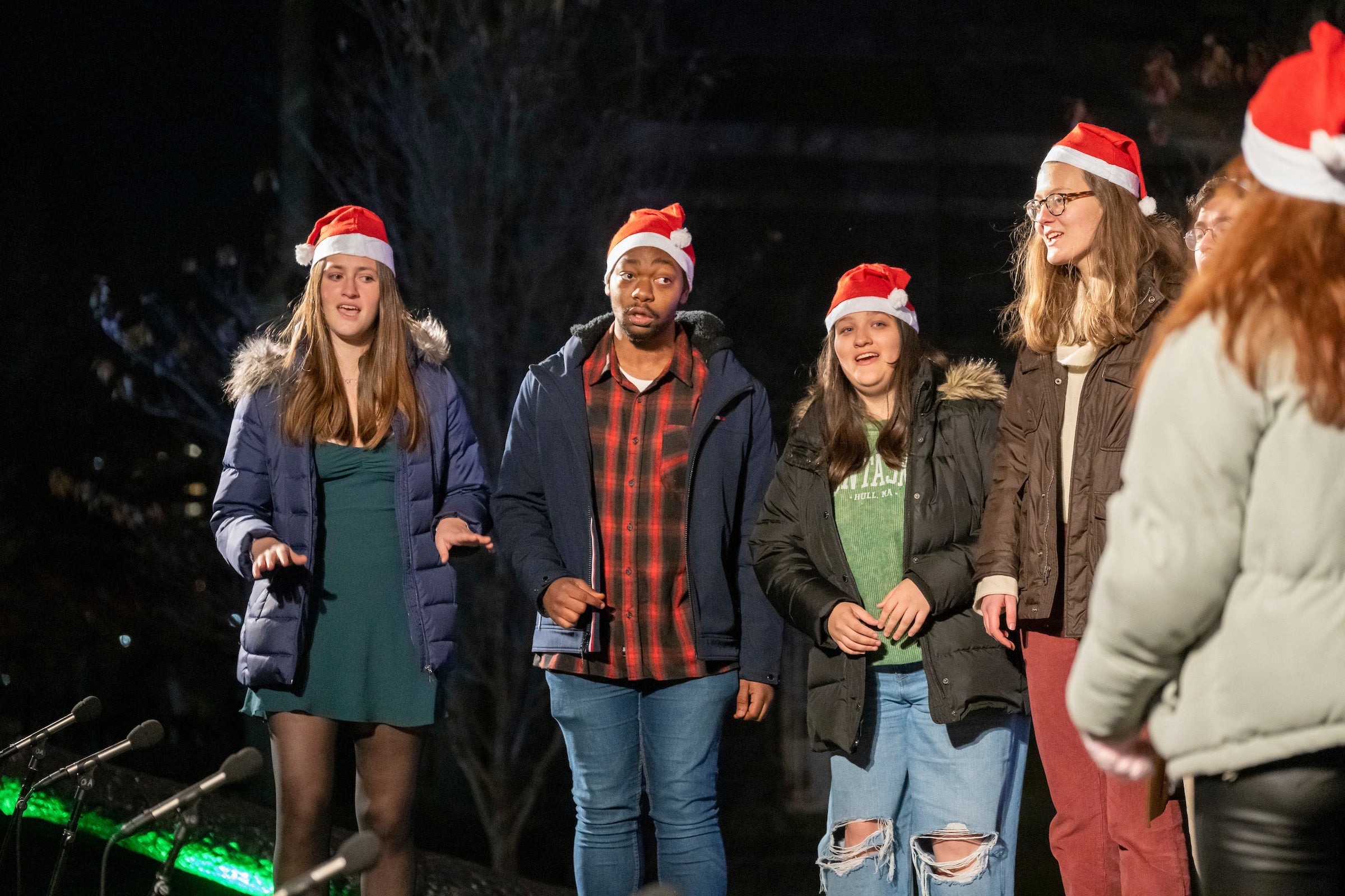 The Georgetown Capitol Gs, a mixed voice acapella group perform. Only 6 are pictured. They are wearing Santa hats.