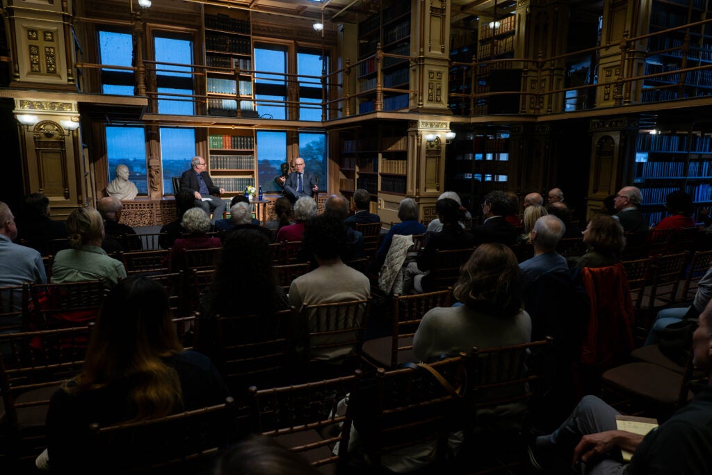 Wide shot of two men sitting in front of a seated audience in the Riggs Library.