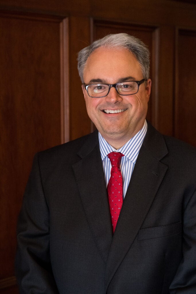 Joe Ferrara, a white man with greying hair and a glasses, wearing a dark suit and red tie.