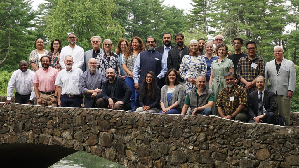 About twenty people of varied races, genders, and ages pose on a stone bridge.