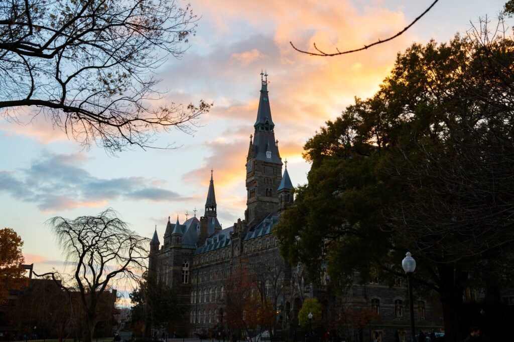 Healy Hall, a Victorian Gothic building, at sunset, framed by trees in the fall that have lost nearly all of their leaves.