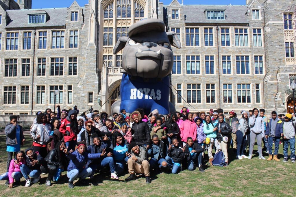 A large group of young, predominantly black students stand in front of Healy Hall. Centered among them is a very large inflatable of Jack the Bulldog.