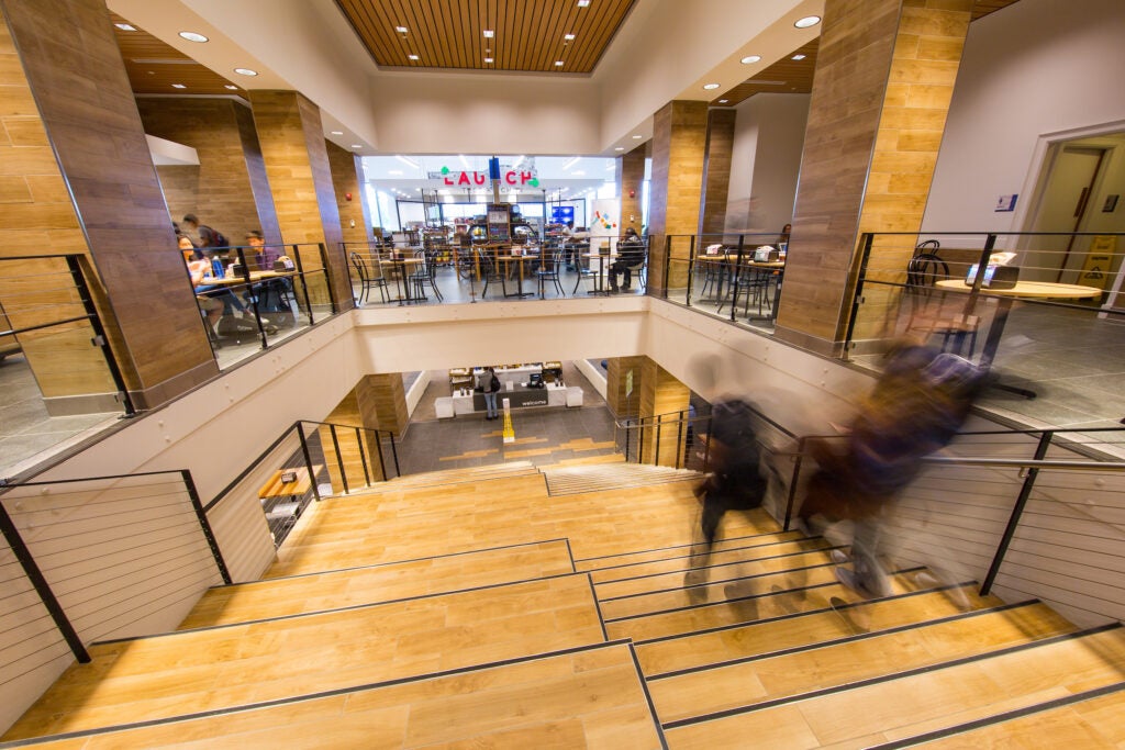 An interior open staircase in an atrium, leading down. Dining hall spaces are visible on both the top and bottom floors.