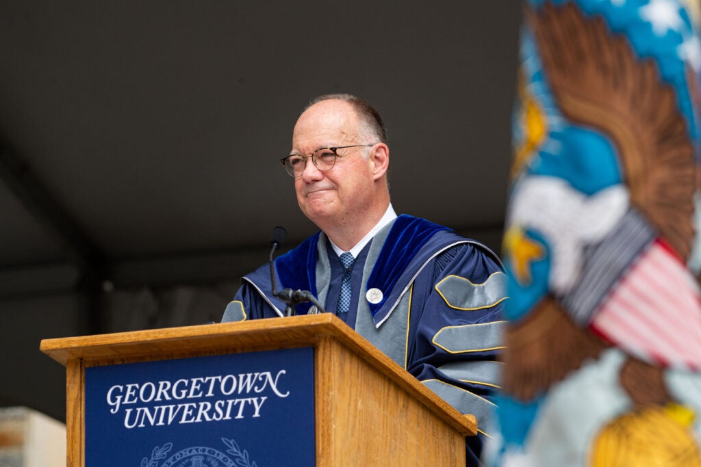 President DeGioia, wearing commencement robes, stands behind a podium.