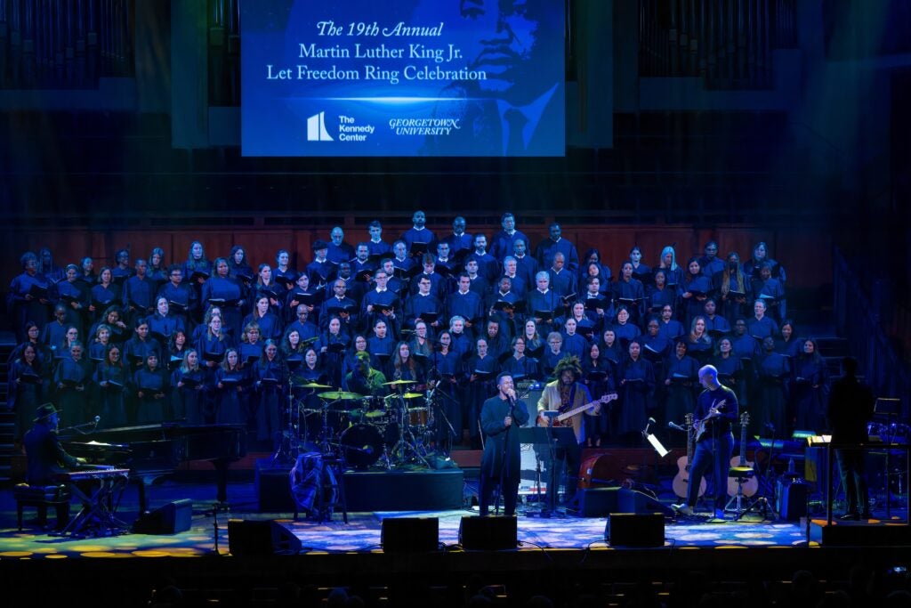 Leslie Odom, Jr. performs in front of a large choir on the Kennedy Center stage