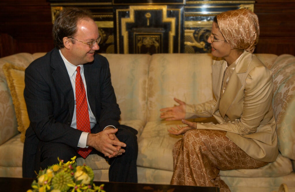 President John J. DeGioia and Her Royal Highness Sheikha Mozah Bint Nasser Al-Missned sit on a couch, engaged in conversation.