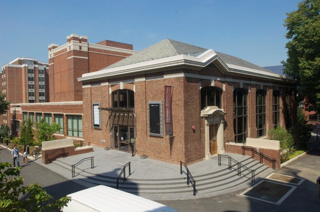 A mid-sized brick building rounds the corner of a pedestrian path. Rounded stairs lead up to the main entrance.