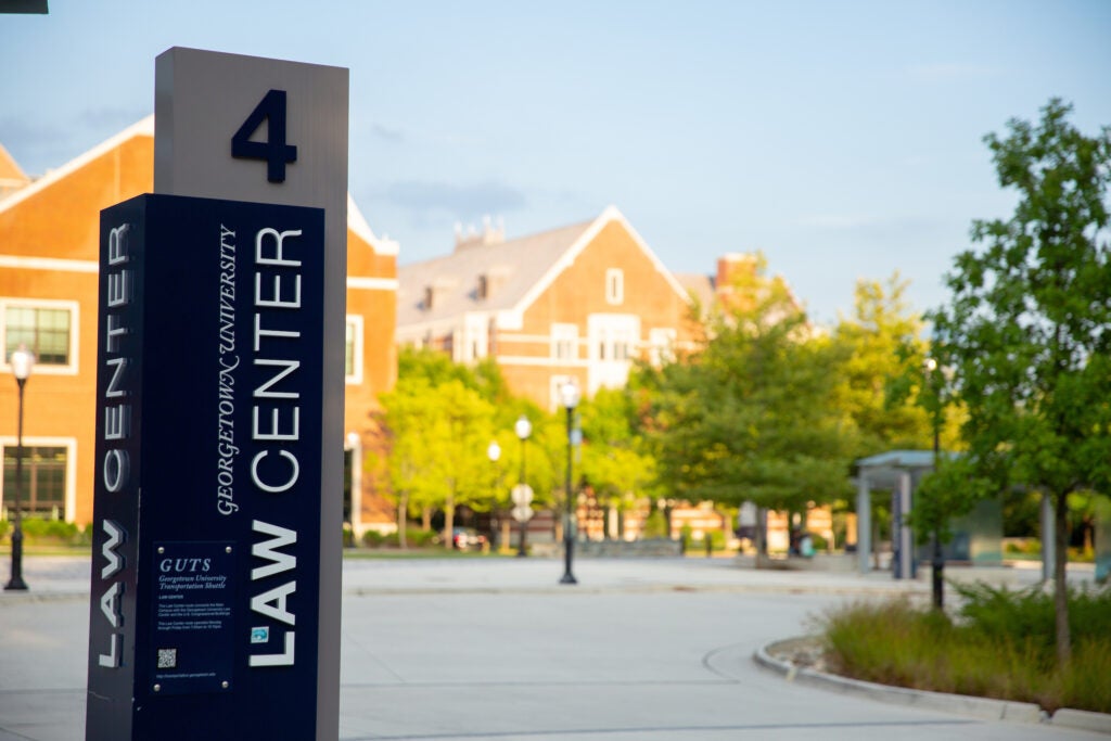 A shuttle bus stop sign for the Georgetown University Law Center, labeled number 4 in a paved bus turn-around, in front of the McDonough Arena.