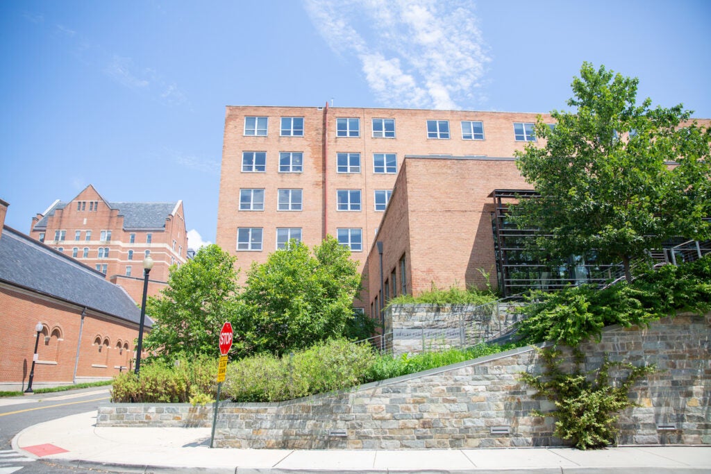 Shorter stone walls surround an outdoor staircase going up and to the right. The stairs sit in front of a tall brick building.