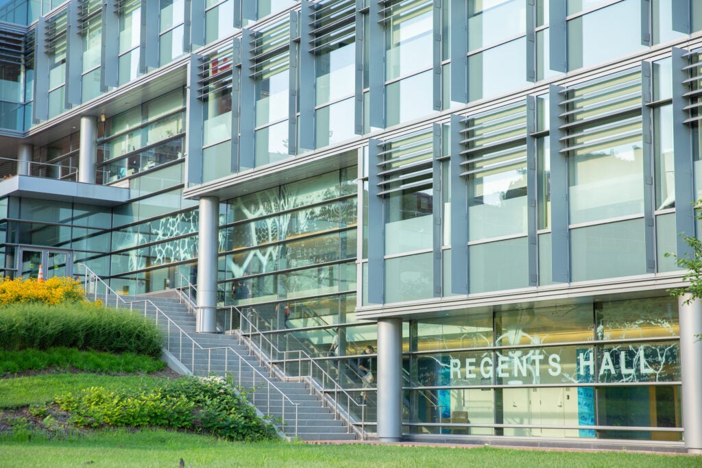 The multi-story, steel and glass facade of Regents hall, facing a hilly, lush green grass garden.