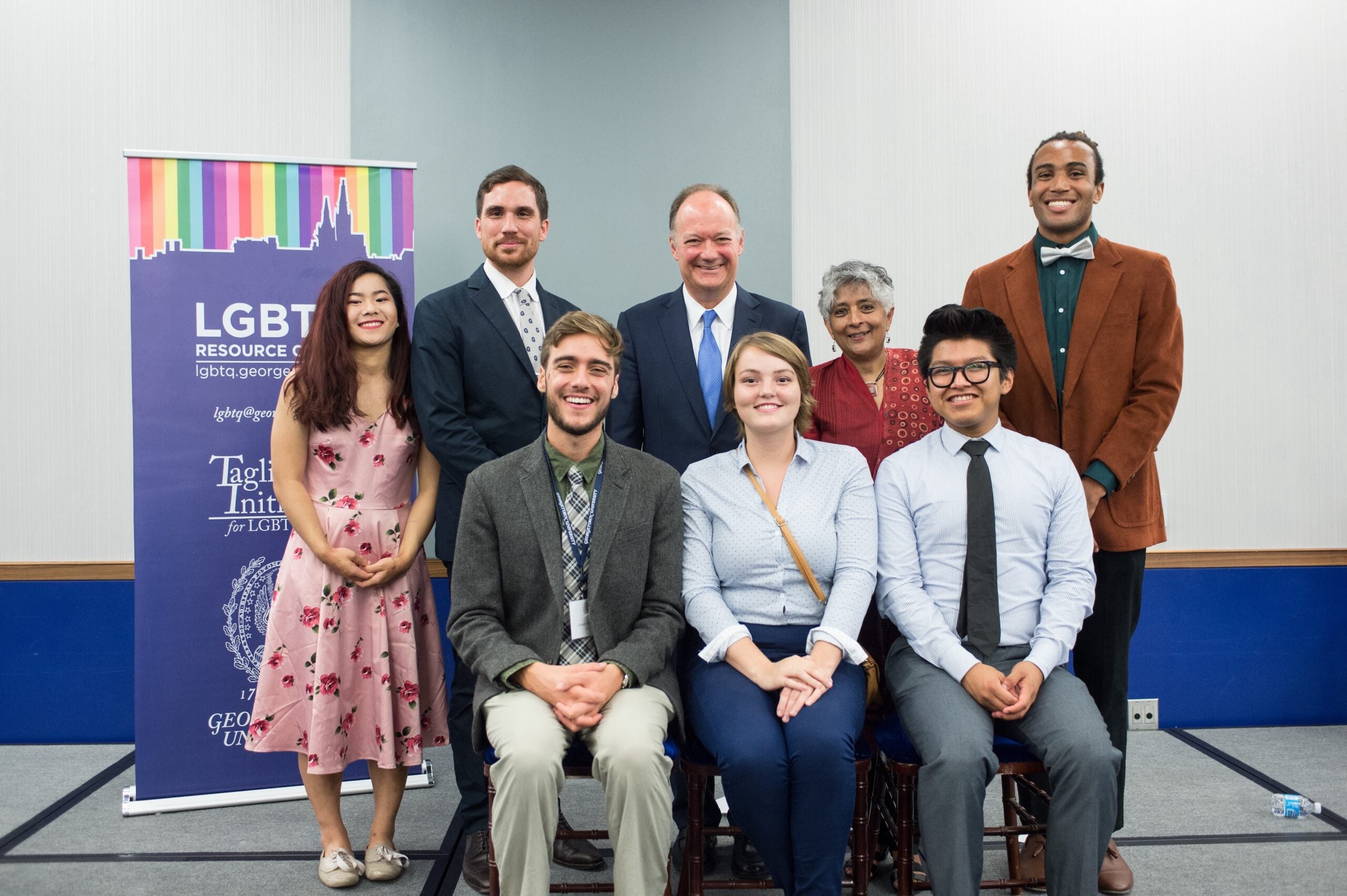 President DeGioia poses among a group of 8 standing and seated people, in front of a banner for the LGBTQ Resource Center.