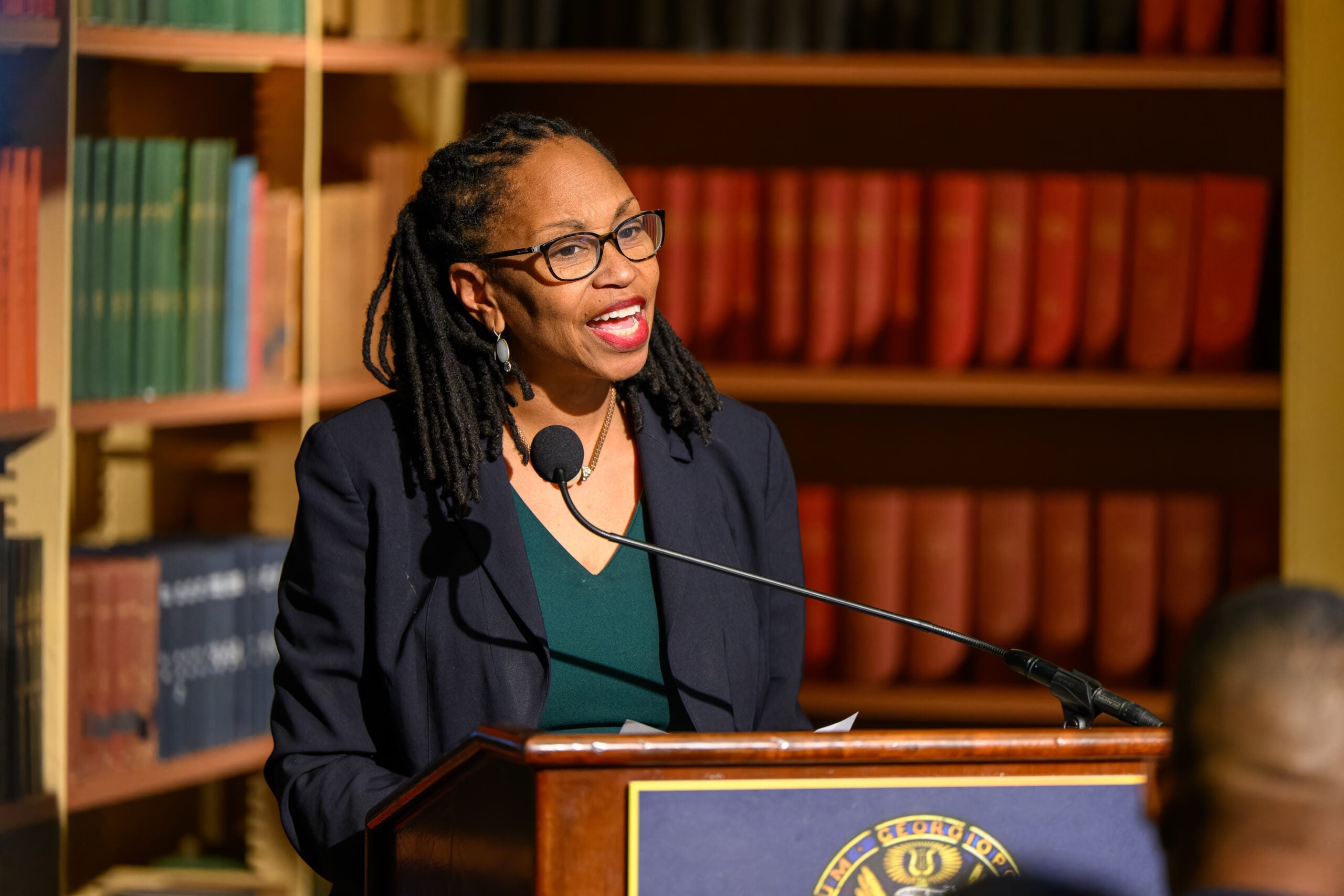 A black woman speaks from behind a podium in Riggs Library.