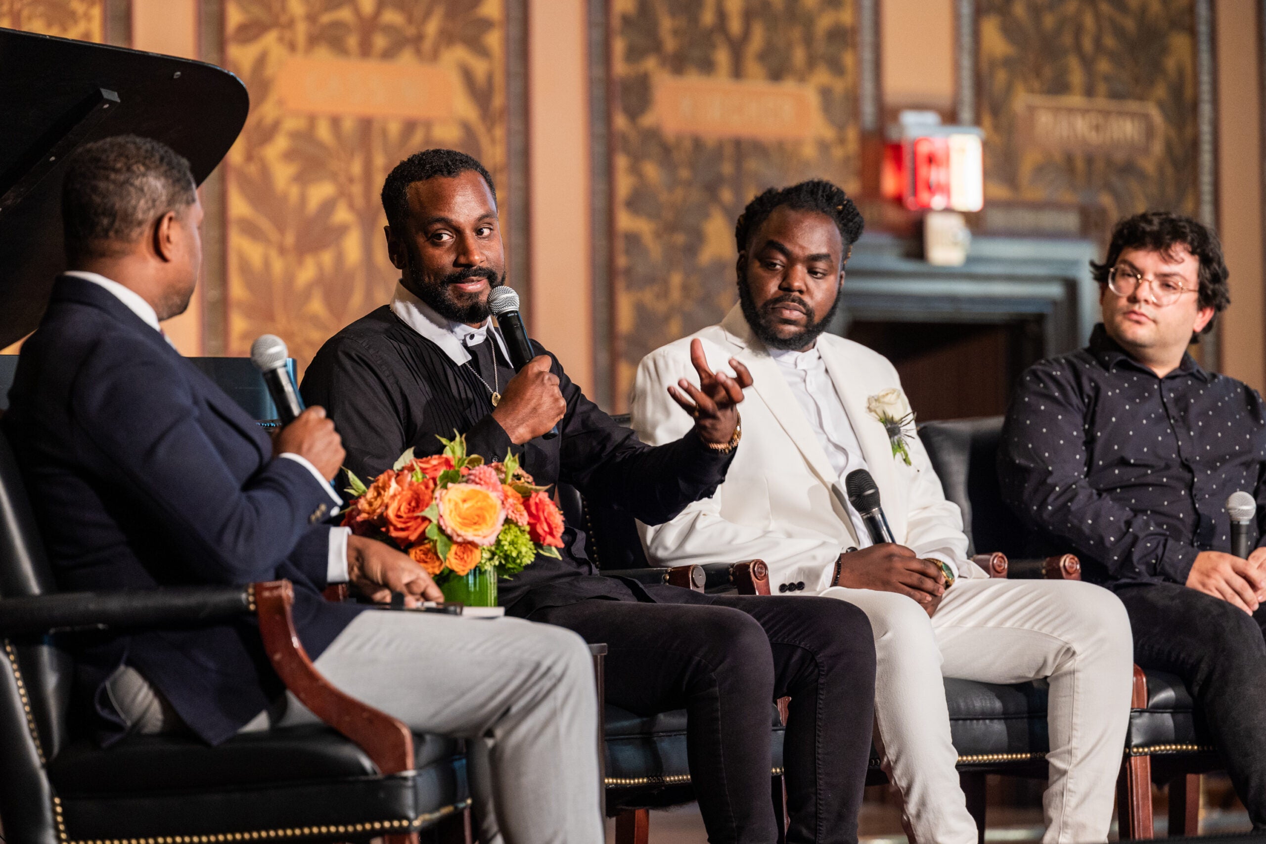 Four people of color sit in conversation on a stage.