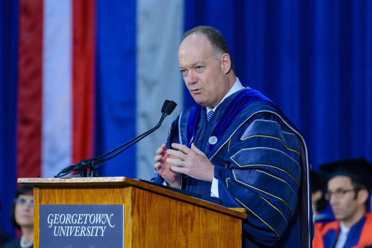 President DeGioia, wearing academic regalia, offers commencement remarks from behind a Georgetown University podium.