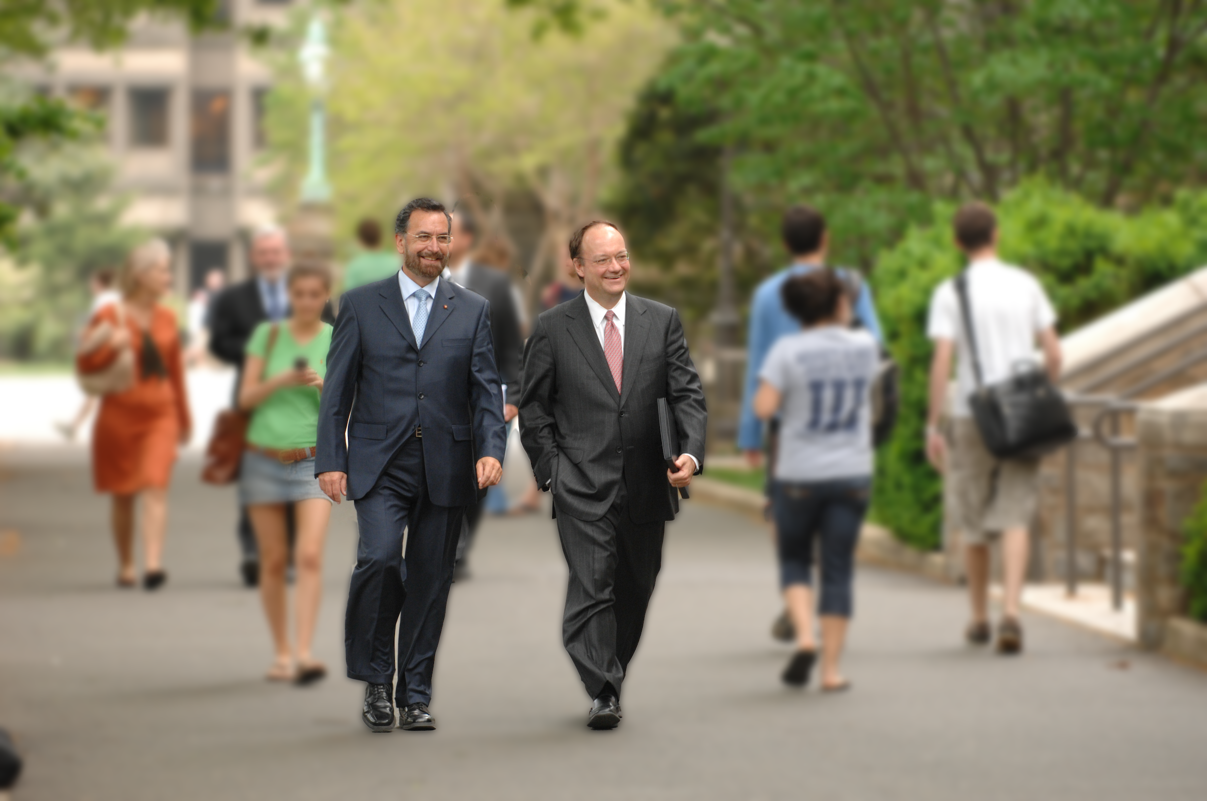 Rabbi David Rosen, KCSG, and John J. DeGioia smile as they walk together through a blurred campus walkway.