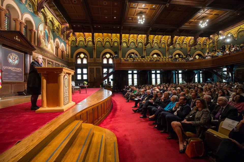 Wide shot of Madeleine Albright speaking to a large seated audience from behind a wooden podium.