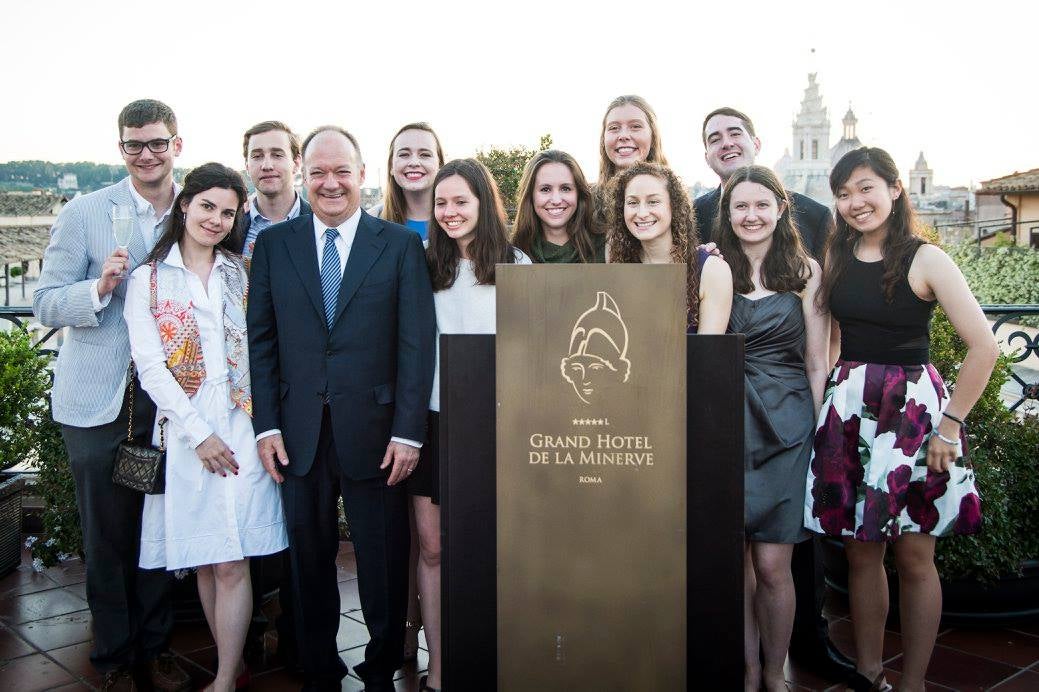President DeGioia poses with a mixed group of students in an outdoor setting around a podium.