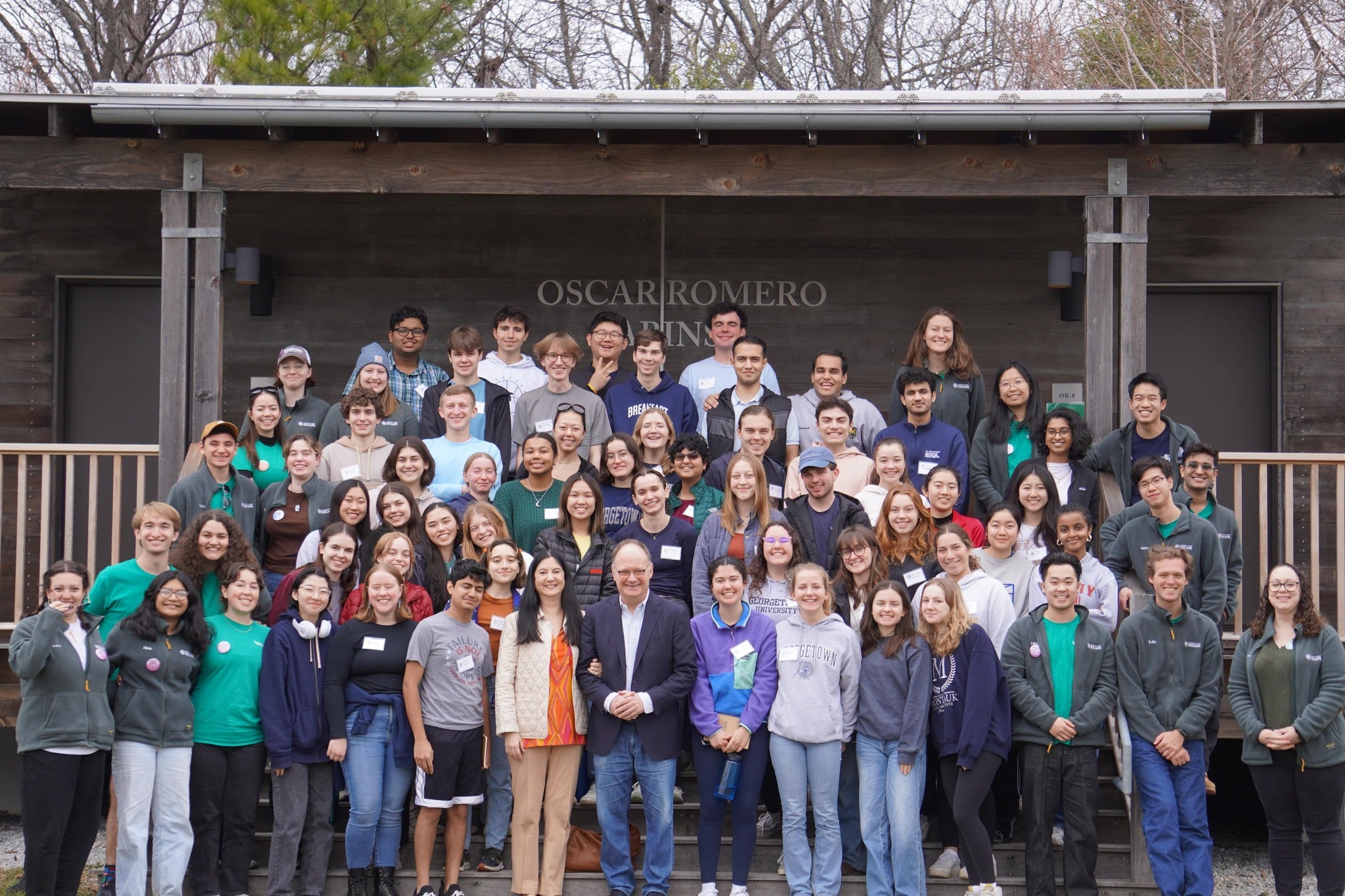 President DeGioia poses with a very large, mixed group of students, standing in a group and facing the camera in front of an outdoor structure.