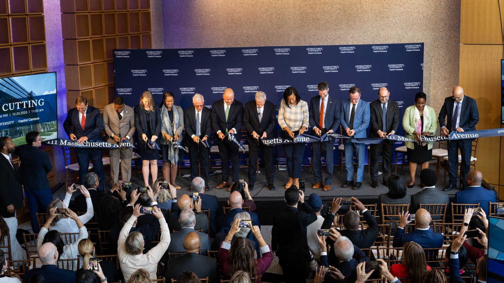 University and Washington DC leaders stand in a row to cut a ribbon in the lobby of a Georgetown University building.