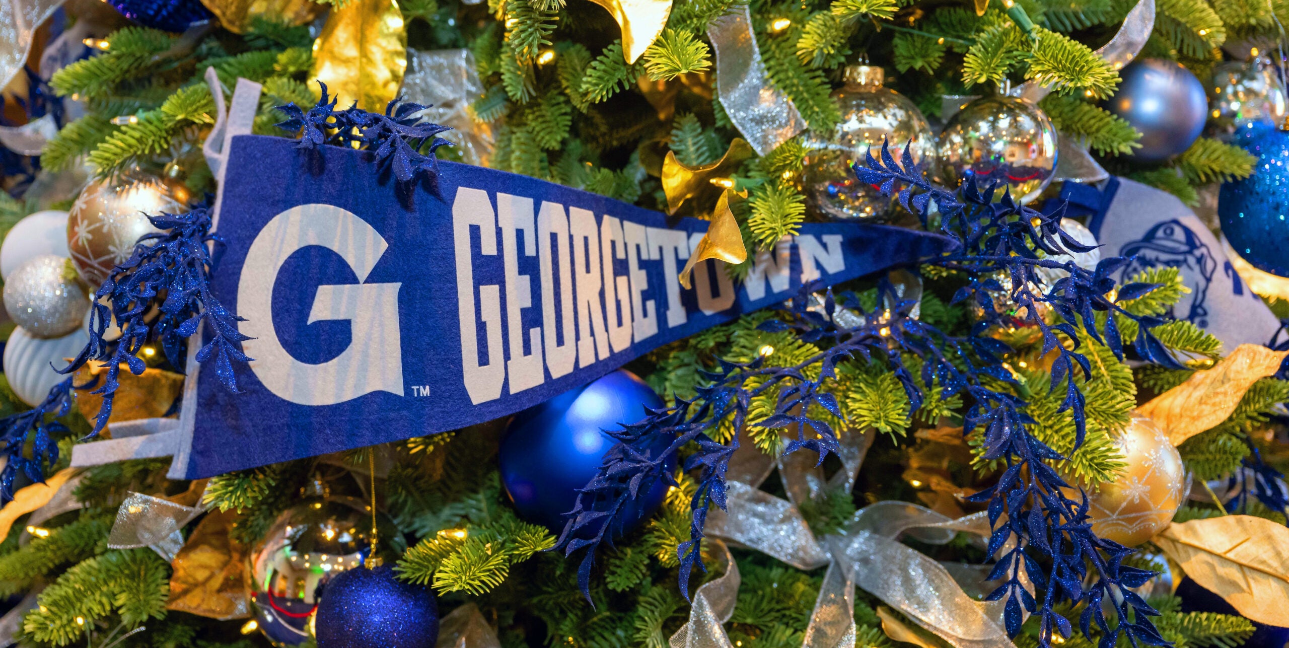 Close up of a decorated Christmas tree, featuring blue and grey ornaments, with a blue and grey Georgetown banner in the center.
