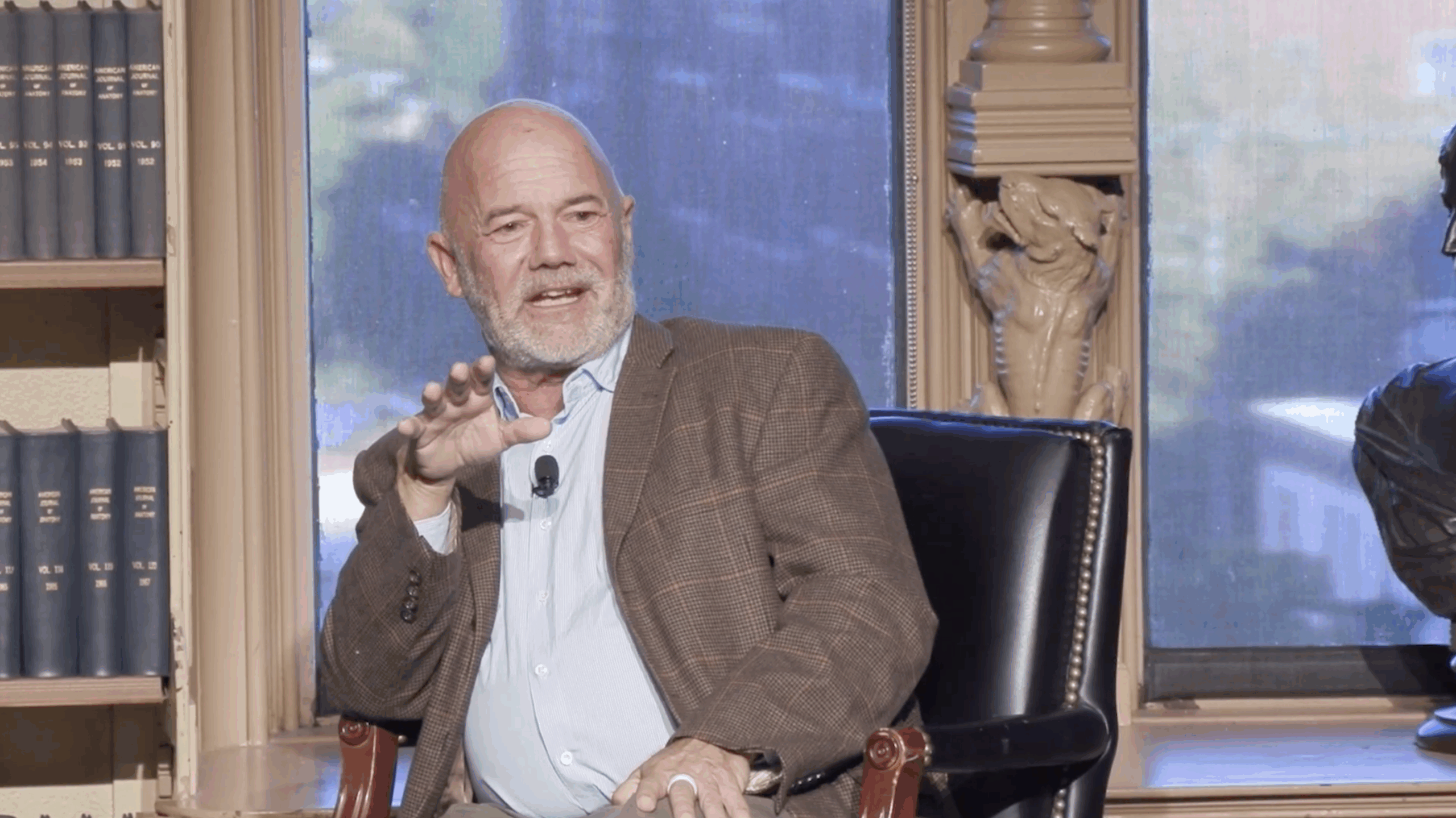 Andrew Sullivan, an older white man with greying facial hair, sits in conversation, speaking to an off-camera audience.