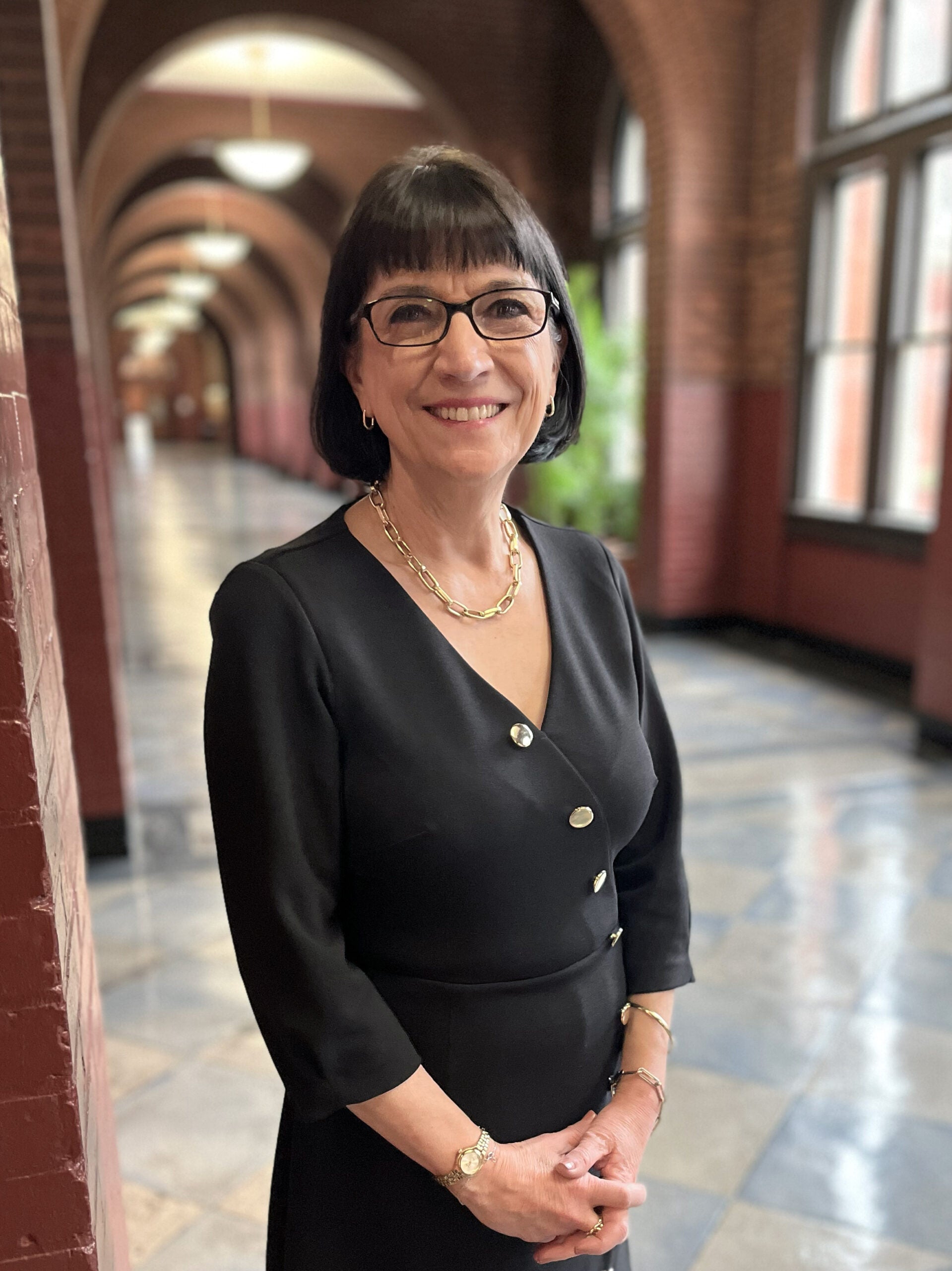 Marie Mattson, a woman with short black hair and glasses wearing a black suit.