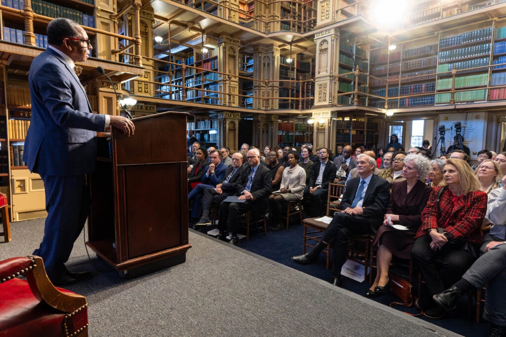 Wide shot of Reynold Verret speaking to a large seated audience in Riggs Library.