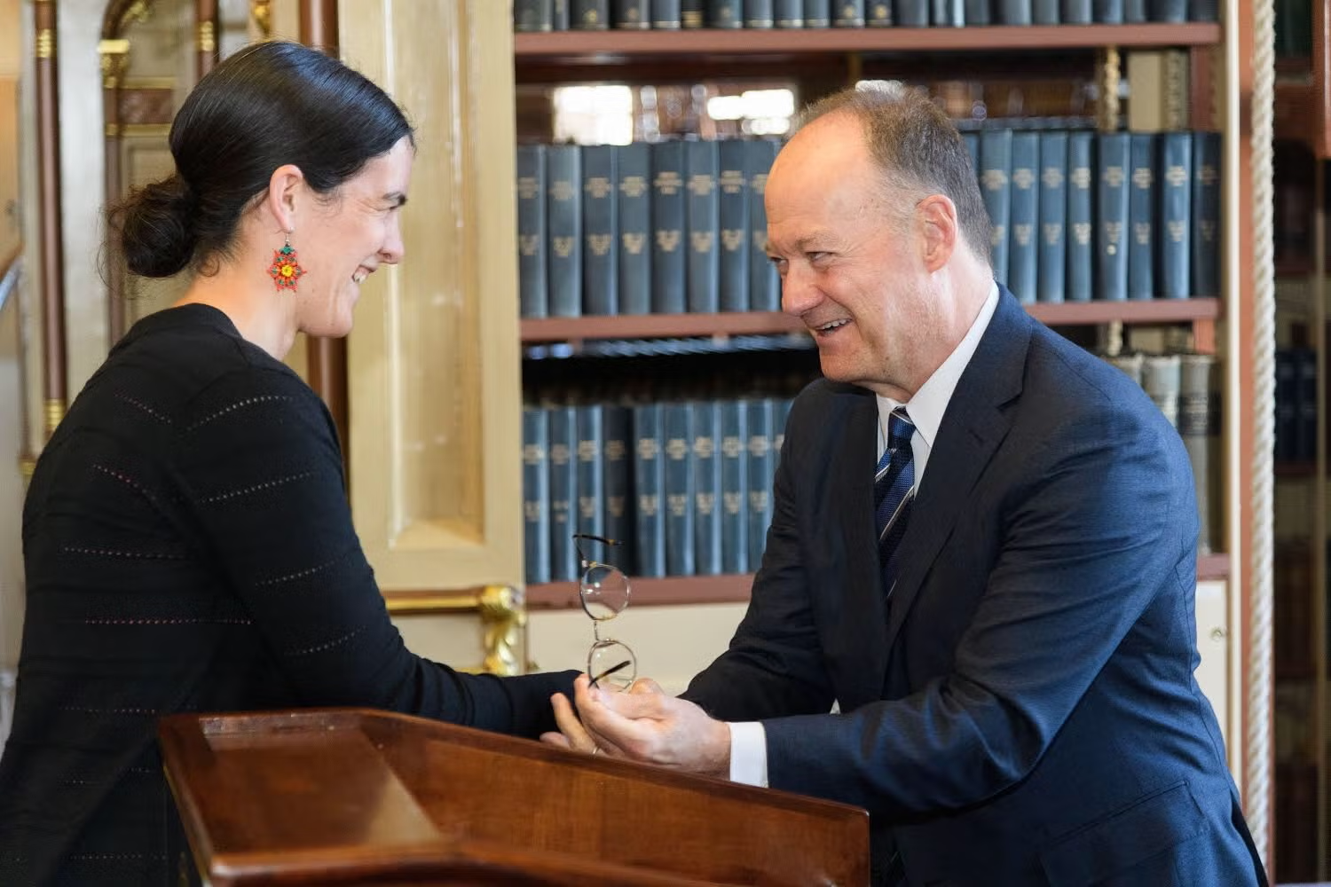 Joanna Foote Williams and then-president John J. DeGioia greet each other behind the podium in Riggs Library.