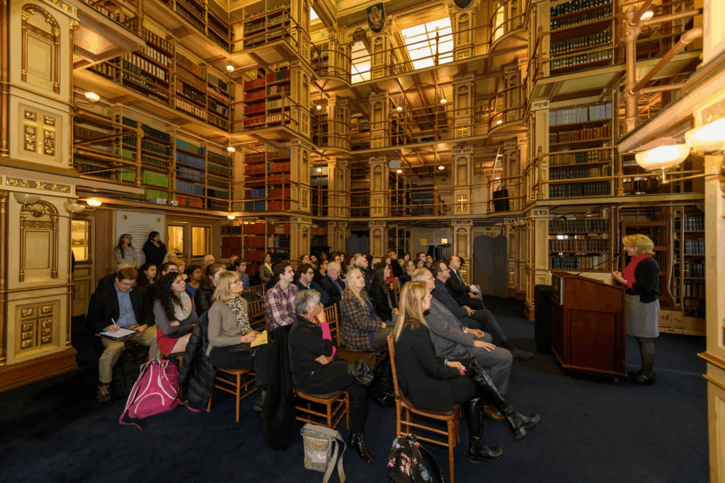 Wide shot of Dr. Nancy Tuchman speaking to a medium-sized seated audience in Riggs Library.