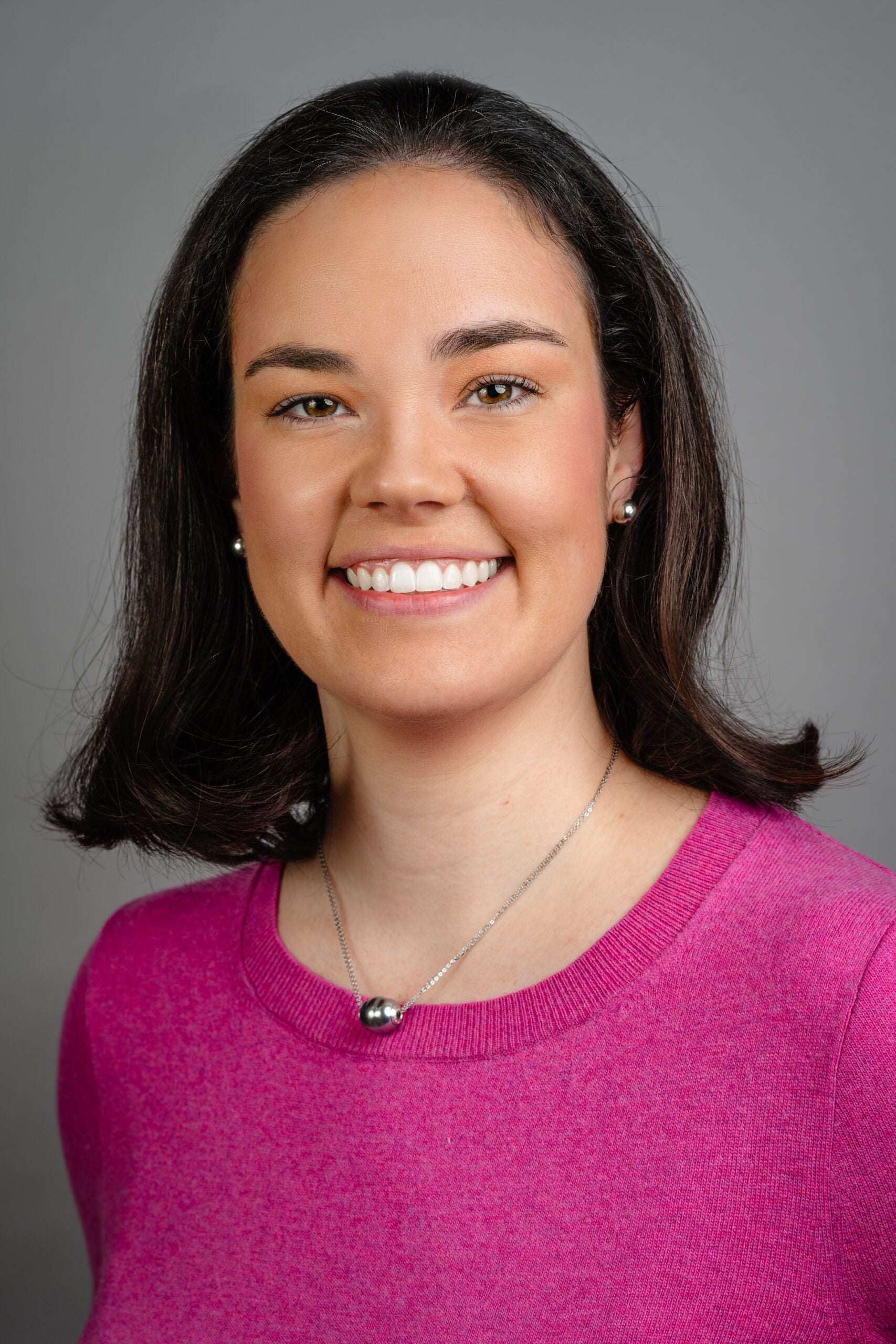 Sarah Nelson, a white woman with long dark hair, wearing a bright pink top.