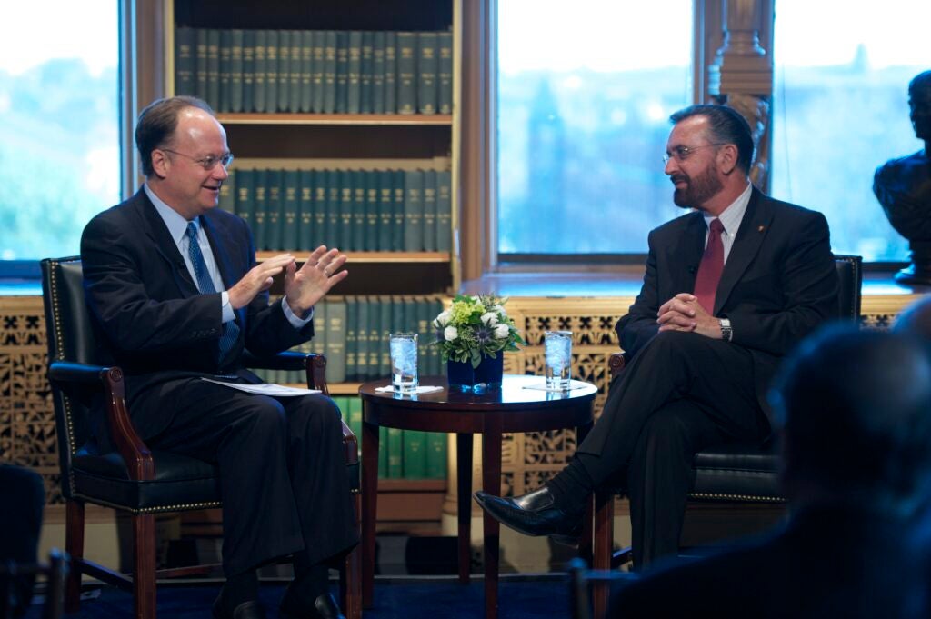 President DeGioia and Rabbi David Rosen, a white man with dark hair and a full beard, wearing a suit, sit while having a conversation. Shelves filled with books line the windowed wall behind them.