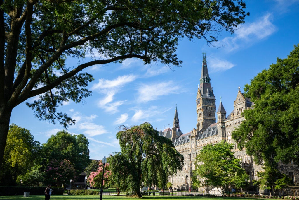 Healy Hall, a neo-gothic stone building, surrounded by leafy green trees under a blue sky in summertime.