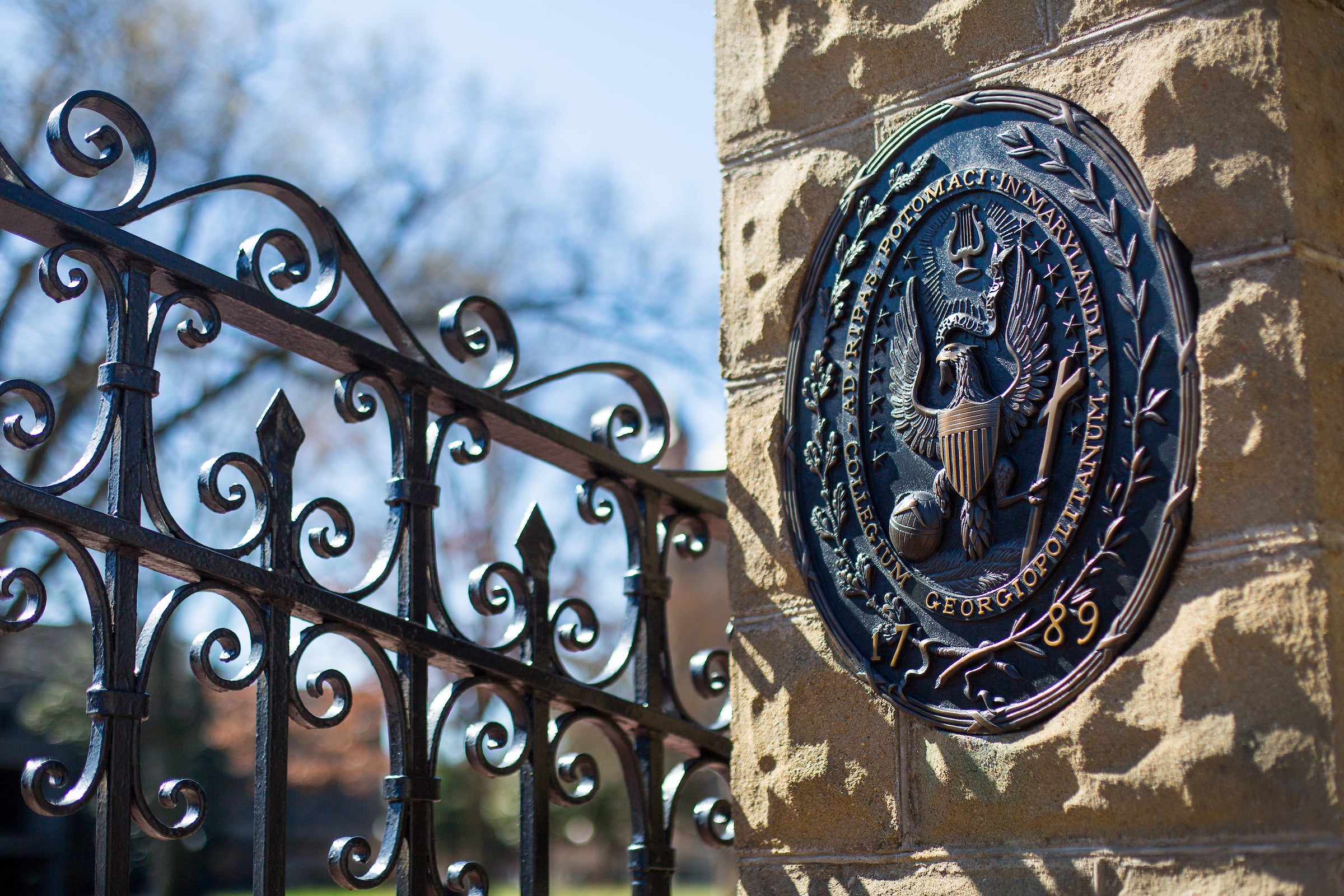 A rendering of the Georgetown University seal in iron, attached to a stone pillar holding an iron gate.