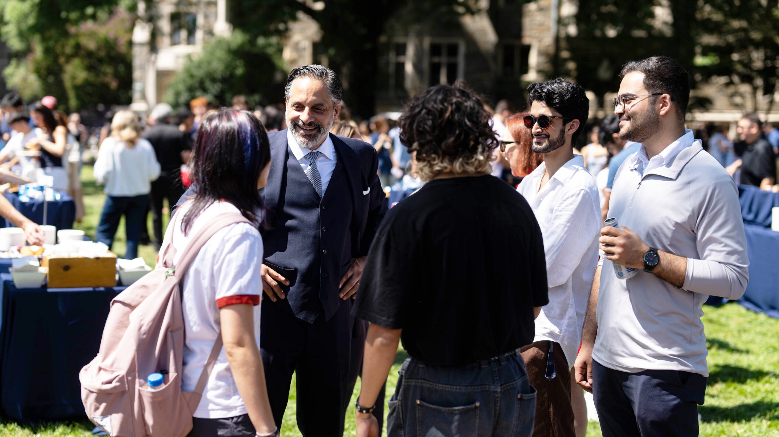 President Peñalver stands on the brick sidewalk in Healy lawn, speaking with a group of students.