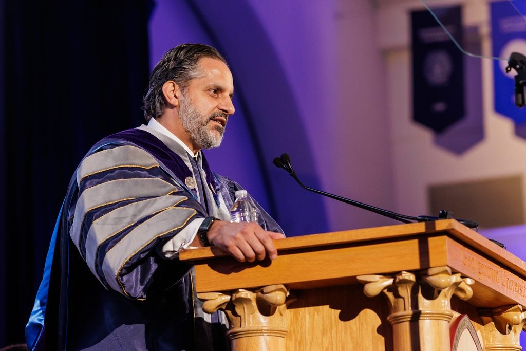 Eduardo M. Penalver, dressed in academic regalia, delivers his inaugural address from behind an ornate wooden podium.